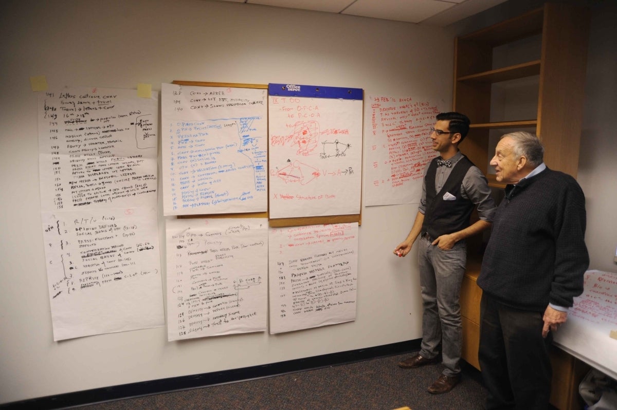 Chris Ali and Elihu Katz standing next to a wall filled with large pieces of paper with many notes tacked to the wall