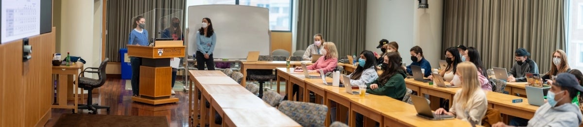 Panorama view of classroom with a student presenting at a podium