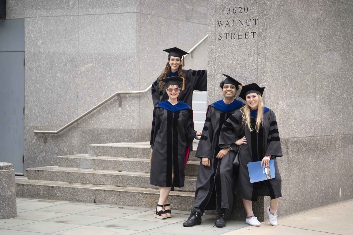 Four graduates in their PhD regalia pose on the steps of 3620 Walnut Street