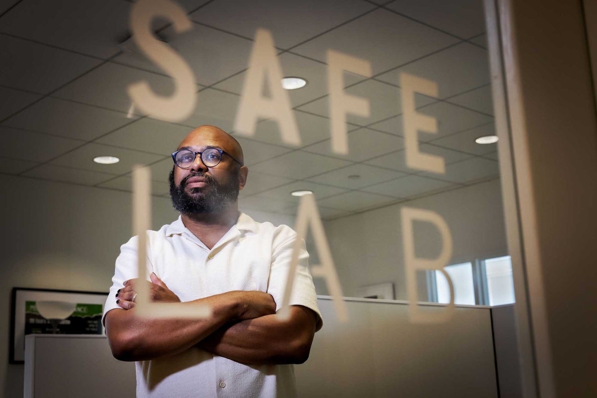 Desmond Patton standing with his arms crossed behind a glass panel reading SAFE Lab