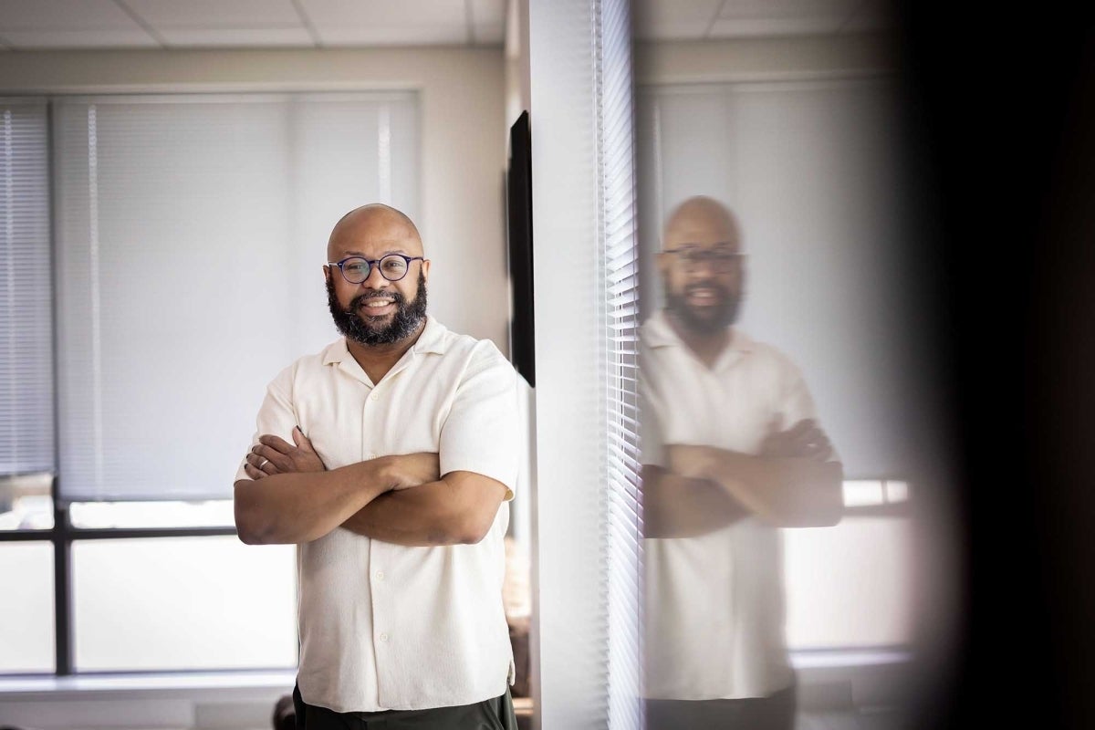 Desmond Patton smiling with his arms crossed while standing in front of a window