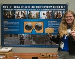Opiod research poster Natalie 700 x 550.jpg Woman holding Narcan and a Google cardboard standing in front of a poster with the headline "A new, free, virtual tool in the fight against opioid overdose deaths"