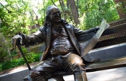 statue of Benjamin Franklin sitting on a bench reading a book, photo credit Scott Spitzer / University of Pennsylvania