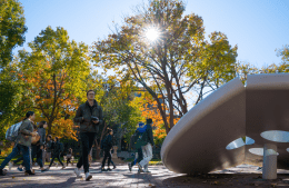 view of students walking past a white modern sculpture of a button on a sunny day 