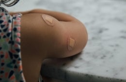 Close up of small child's arm with small circular band aids on it, photo credit Charles Deluvio / Unsplash