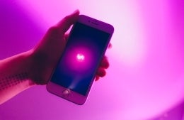 Closeup of hand holding a phone that shows the word Lyft glowing in pink, photo credit Thought Catalog / Unsplash