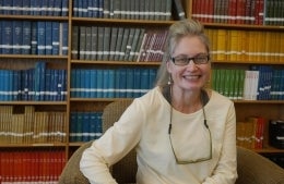 Sharon Black sitting on a chair with bookshelves in the back