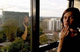 Eleanor Marchant standing in front of a window that that has the view of a city from a high level. There are trees and buildings in view.