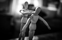 Two wooden dolls in black and white, one holding the other, the other with its arms out; photo credit: Charl Folscher / Unsplash