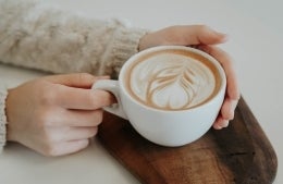 Latte in a white latte cup on a piece of dark wood; photo credit: Christiana Rivers / Unsplash