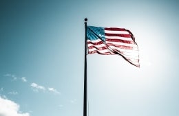 American flag waving against sky in front of sun; photo credit: Justin Cron / Unsplash