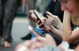 3 people on their phones, with the person in the middle in focus, in public area with surroundings blurred; photo credit: Robin Worrall / Unsplash