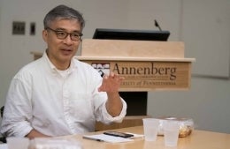 Guobin Yang seated at a table talking with an Annenberg podium behind him