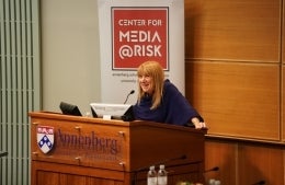 Barbie Zelizer standing behind a podium and speaking.