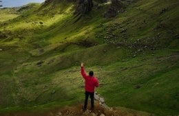 man standing in nature with his left hand up, making a peace sign, photo credit Michael Block/Pexels