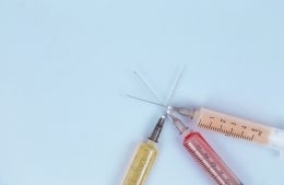 three syringes with different color liquids on a blue background; Photo by Diana Polekhina on Unsplash