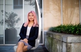 Woman with pink hair sitting on a bench outdoors and looking at the camera