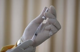 Gloved hands drawing a medication into a syringe from a vial