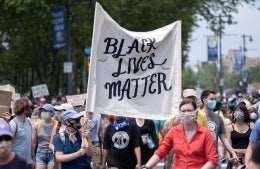 Protestors wearing COVID-protective facemasks march holding Black Lives Matter signs
