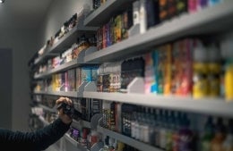 Shelves lined with colorful boxes and vials, with a hand reaching up. Labels are blurred.