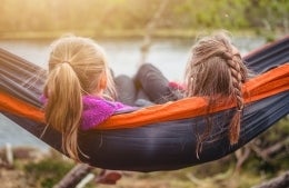 Two women sitting on a hammock and looking towards a lake. Photo Credit: Janko Ferlič / Unsplash