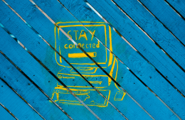 Yellow graffiti on blue wood slats of desktop computer with the words "Stay Connected" written on the monitor