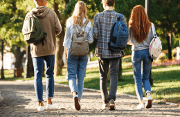 4 college-aged students wearing backpacks walk down a path