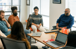 SAFELab researchers sit in a circle of chairs in a conference room