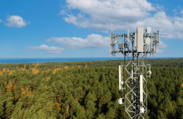 Telecommunication tower with cellular antennas for 5g mobile internet network stands in a forest with a blue sky background