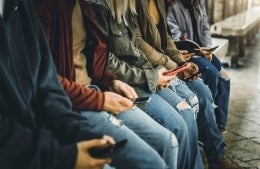 Five people sit on a bench looking at their smart phones 