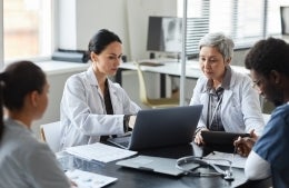 two doctors looking at a laptop next to two doctors sitting at a table