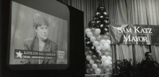 Large screen showing Kathleen Hall Jamieson, dean of the Annenberg School, with a bunch of balloons and a sign reading "Sam Katz, Mayor"