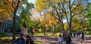 People walking around on the University's campus pathways with fall trees around them