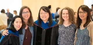 Five women posing together, two in graduation regalia
