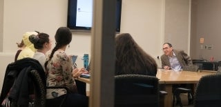 Joseph Turow seated at a table with students, viewed from outside the classroom