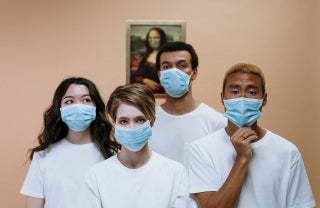 Four people in white t-shirts and blue face masks standing in front of a Mona Lisa replica that is wearing a face mask