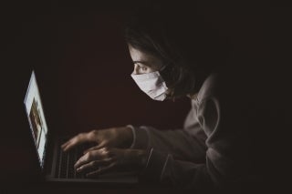 Woman wearing a mask reading from a laptop in the dark