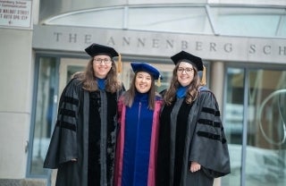Three graduates in regalia posing in front of the Annenberg School
