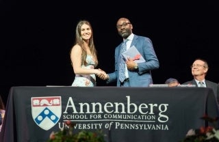 Dean Jackson shaking hands with a student in front of a table with an Annenberg logoed tablecloth