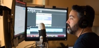 Man siting in front of a microphone and several monitors