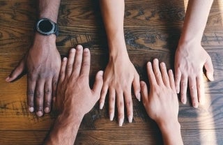 Abstract photo of different sizes and colored hands next to each other on a table; photo credit: Clay Banks / Unsplash