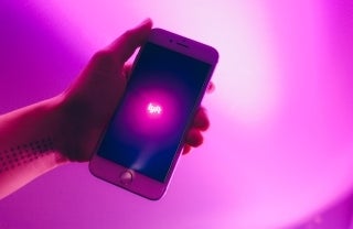 Closeup of hand holding a phone that shows the word Lyft glowing in pink, photo credit Thought Catalog / Unsplash