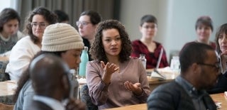 Woman speaking while seated amid many other people