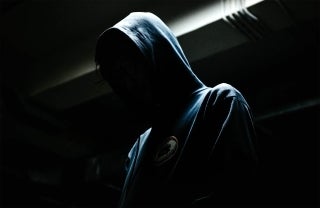 Hooded figure in a dimly lit area, photo credit @rendiansyah / Unsplash