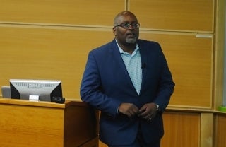 Eric Deggans leaning on a wooden podium at the front of a lecture theater