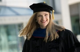 Ph.D. graduate smiling for the camera in black cap with yellow tassel and black gown. 