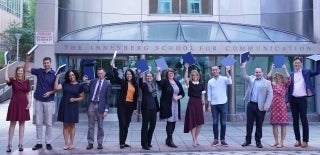 a line of alumni holding their bound dissertations in the air in front of the Annenberg School