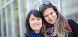 Two graduates posing in front of a glass wall