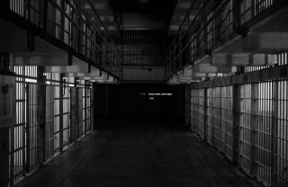 Black and white image of the inside of a prison with cells on each side, photo credit Emiliano Bar / Unsplash