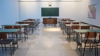 Classroom with lines of green desks and wooden chairs to the left and right of the room. In the middle of the room, there is a teacher's desk made of women that is in front of a green chalk board; photo credit: Ivan Aleksic / Unsplash
